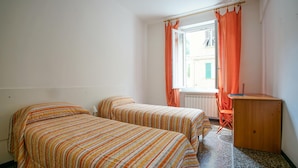 A room with two single beds, a wooden desk, and a window with orange curtains.