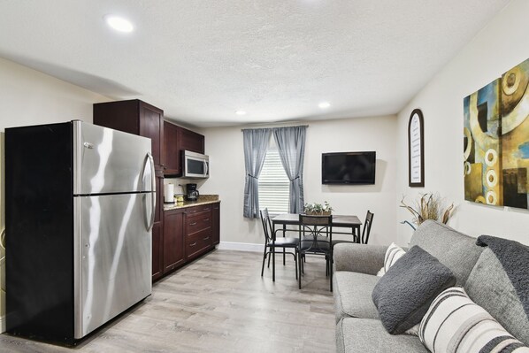 A compact living space with a kitchenette, dining area, and a gray sofa with striped cushions.
