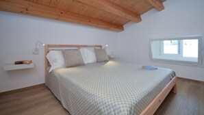 Ein Schlafzimmer mit Holzbalkendecke, einem Bett mit gemustertem Überwurf, einem Nachttisch mit Lampe und einem Fenster mit Blick.