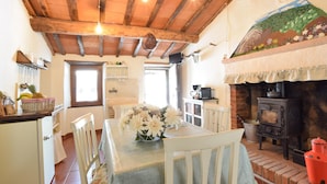 Une cuisine rustique avec un plafond en bois, une cheminée en briques et un coin repas où une table est dressée pour deux personnes.
