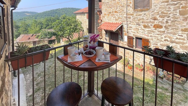 Un balcon avec une table dressée pour deux personnes, donnant sur un bâtiment en pierre et un paysage verdoyant.