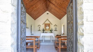 Uma capela com teto de madeira, paredes de pedra, altar central e dois bancos.