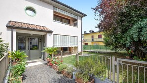 A two-story building with a tiled roof, a balcony, and a paved courtyard with potted plants. - Appartamento Signoretti (Pieve di Soligo)