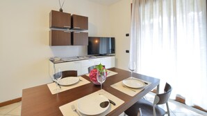 A modern kitchen with dark wooden cabinets, a flat-screen TV, and a dining area with a table set for two. - Appartamento Signoretti (Pieve di Soligo)
