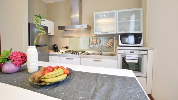 A modern kitchen with white cabinets, a gas stove, a microwave, and a stainless steel range hood. - Appartamento Signoretti (Pieve di Soligo)