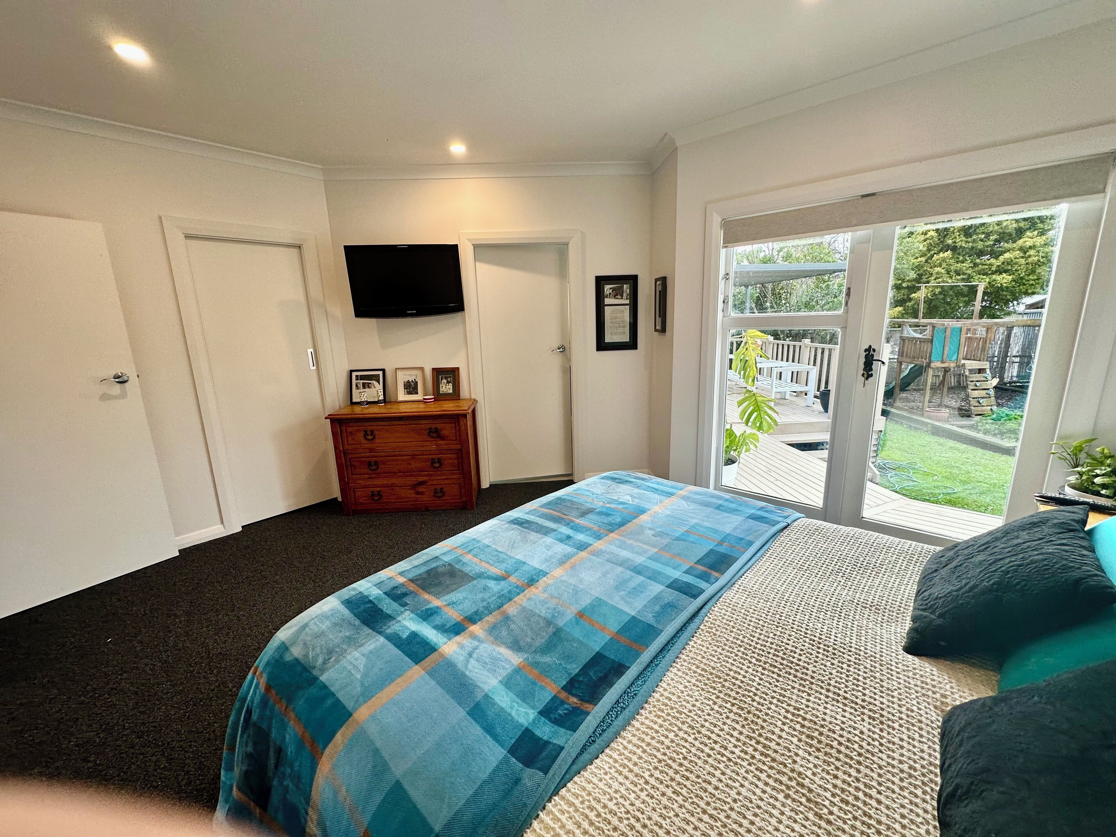 A bedroom with a bed, a dresser, a television, and a sliding glass door to a backyard.