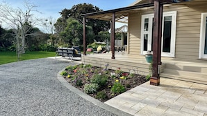 En täckt uteplats med utemöbler, en trädgård med färgstarka blommor och ett hus med beige fasadpanel och vita detaljer.