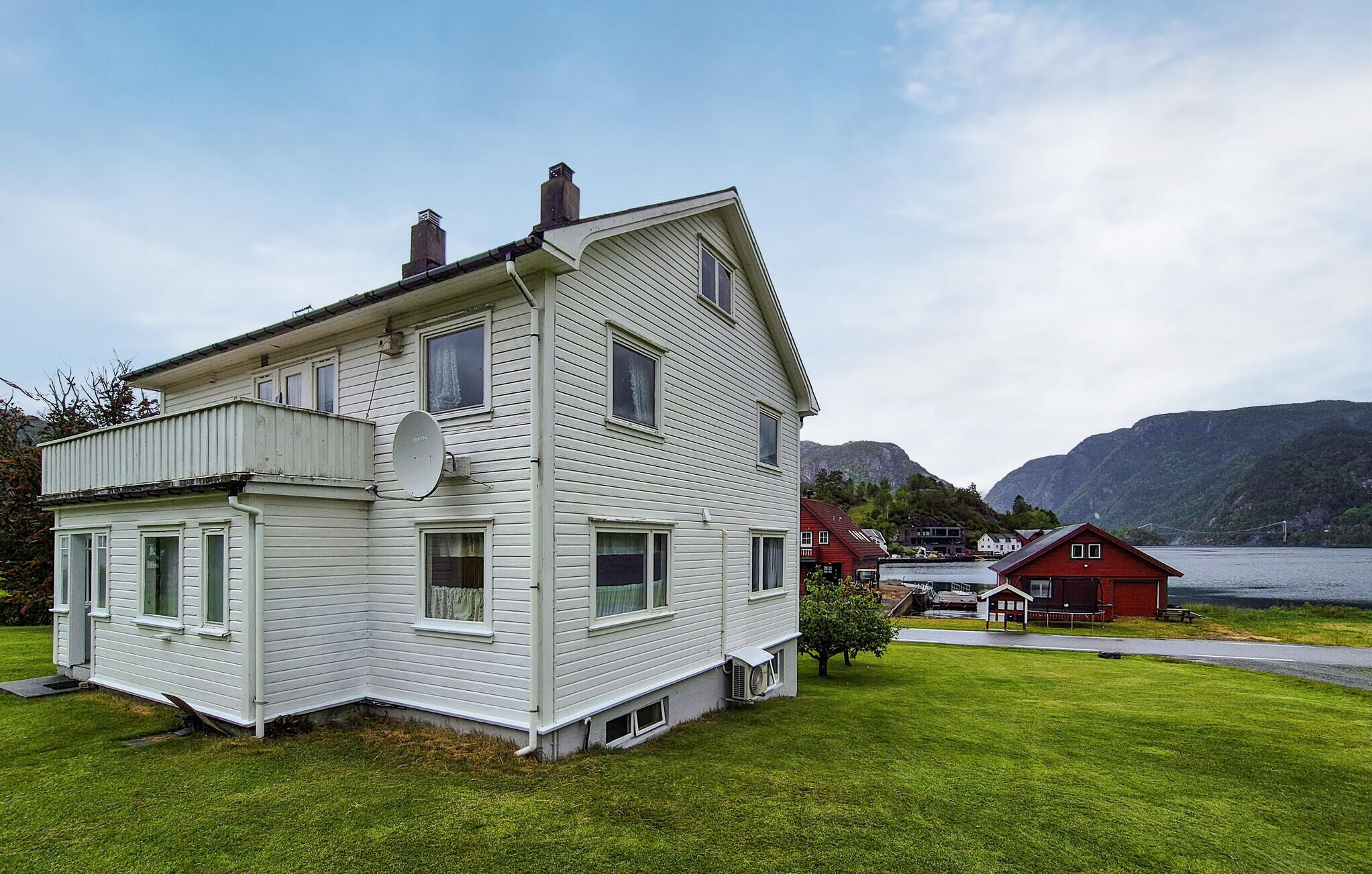 Een huis met twee verdiepingen, een schotelantenne, een klein terras en uitzicht op een meer en bergen op de achtergrond.