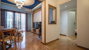 Una habitación moderna con suelo de madera, un área de comedor con una mesa y sillas, un televisor sobre un mueble bajo y un espejo en la pared.