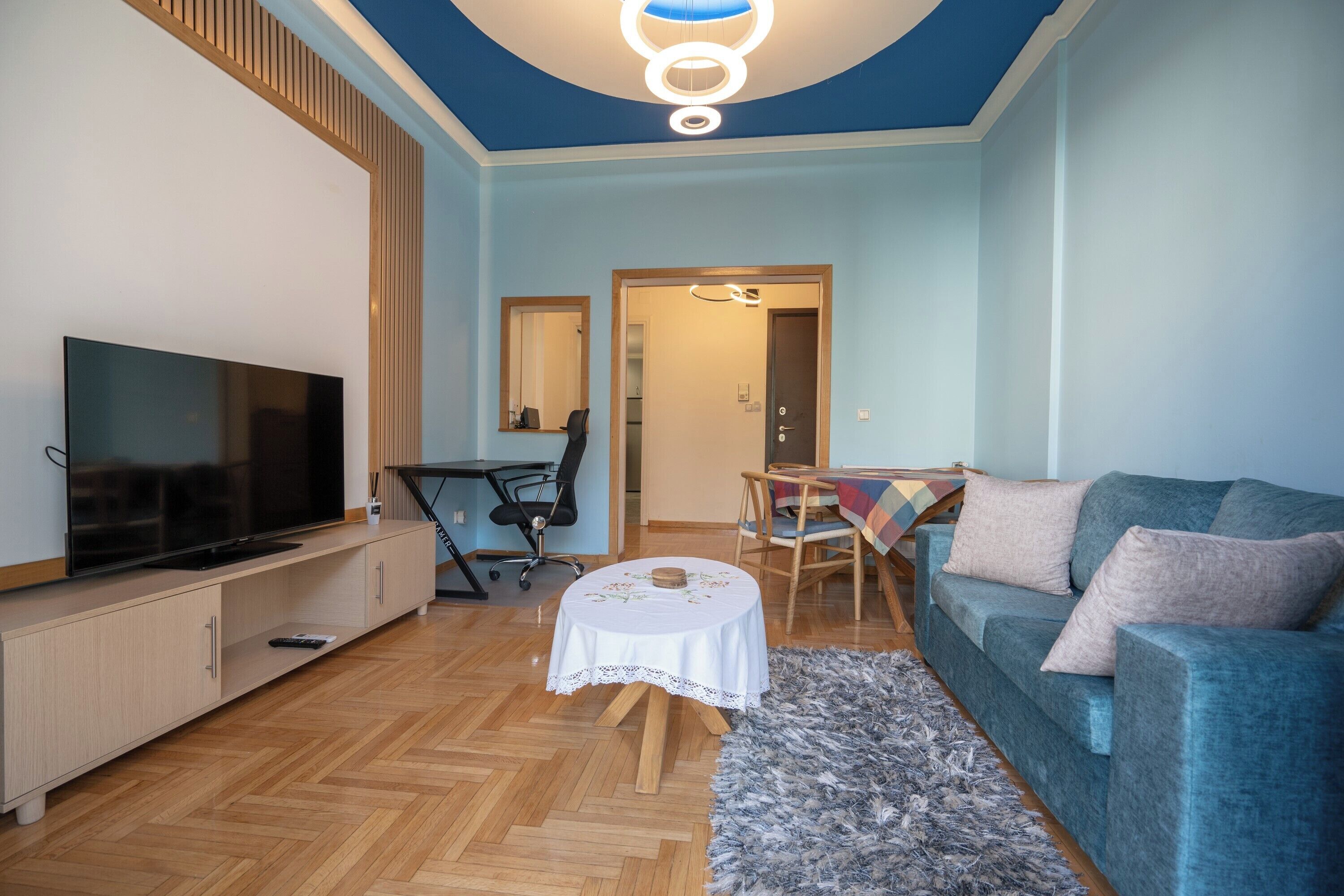 En moderne stue med et fladskærms-tv, en blå sofa, et lille rundt bord og et træskab.