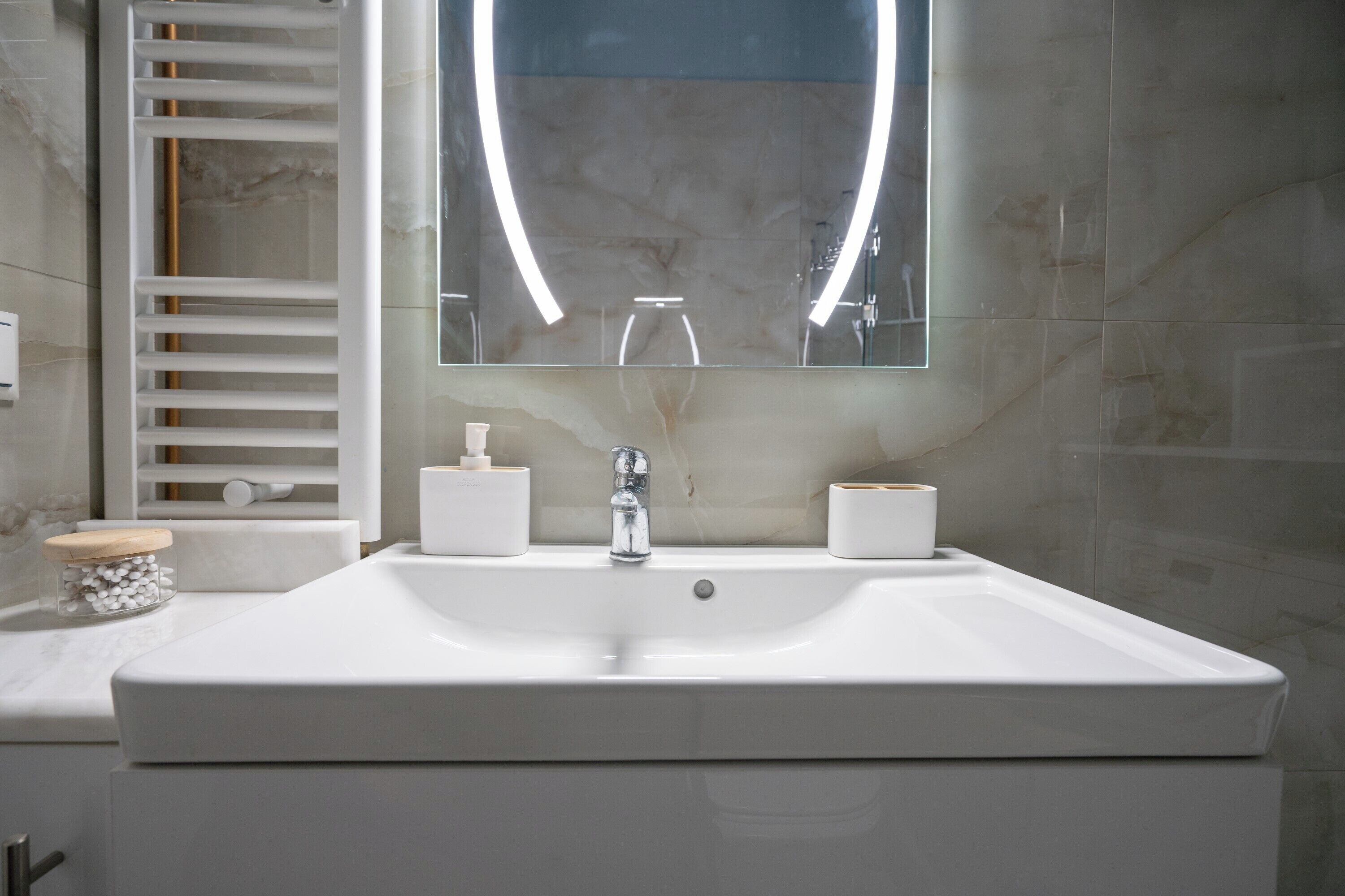 A modern bathroom with a large white sink, a mirror with a lighted frame, and a towel rack.