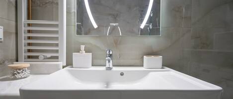 A modern bathroom with a large white sink, a mirror with a lighted frame, and a towel rack.