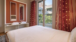 Un dormitorio con una cama grande, una mesita de noche con toallas, un espejo y una ventana con cortinas.