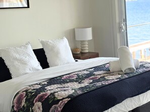Ein Bett mit floralem Überwurf, weißen Kissen und einem zusammengerollten Handtuch.