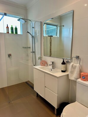 Ein modernes Badezimmer mit Duschkabine aus Glas, einem weißen Waschtisch mit Spiegel und einer Toilette.