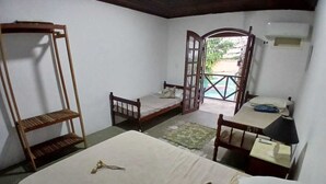 Une pièce comprenant un lit, un banc en bois, une petite table avec une lampe et une porte ouverte donnant sur l’extérieur.