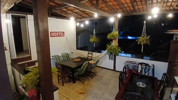 Une chambre d’auberge de jeunesse comprenant un coin repas, un lit et une fenêtre ornée de plantes suspendues.