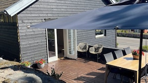 Una casa moderna con un patio, mobiliario exterior y un gran paraguas.