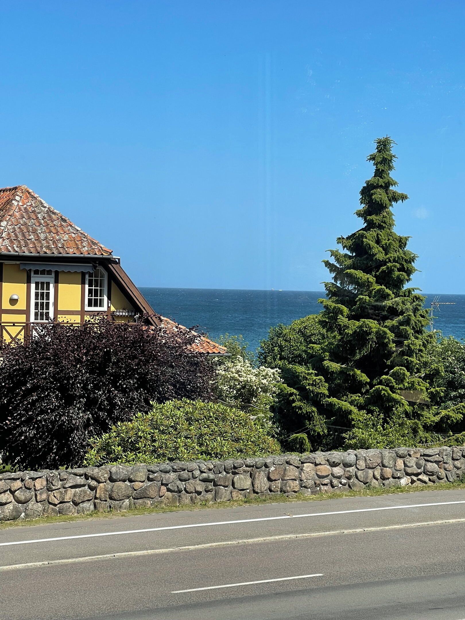 Una casa costera con un muro de piedra, un camino en primer plano y una vista despejada del mar.