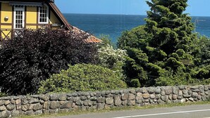 Una casa costera con un muro de piedra, un camino en primer plano y una vista despejada del mar.