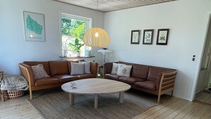 Una sala de estar con una mesa redonda, dos sofás de cuero marrón, techo de madera y un ventanal grande.