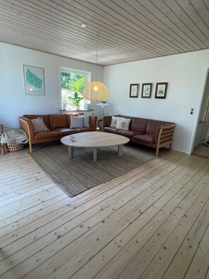 Un salon avec une table basse ronde, deux canapés en cuir marron, un plafond en bois et une fenêtre donnant sur un paysage verdoyant.