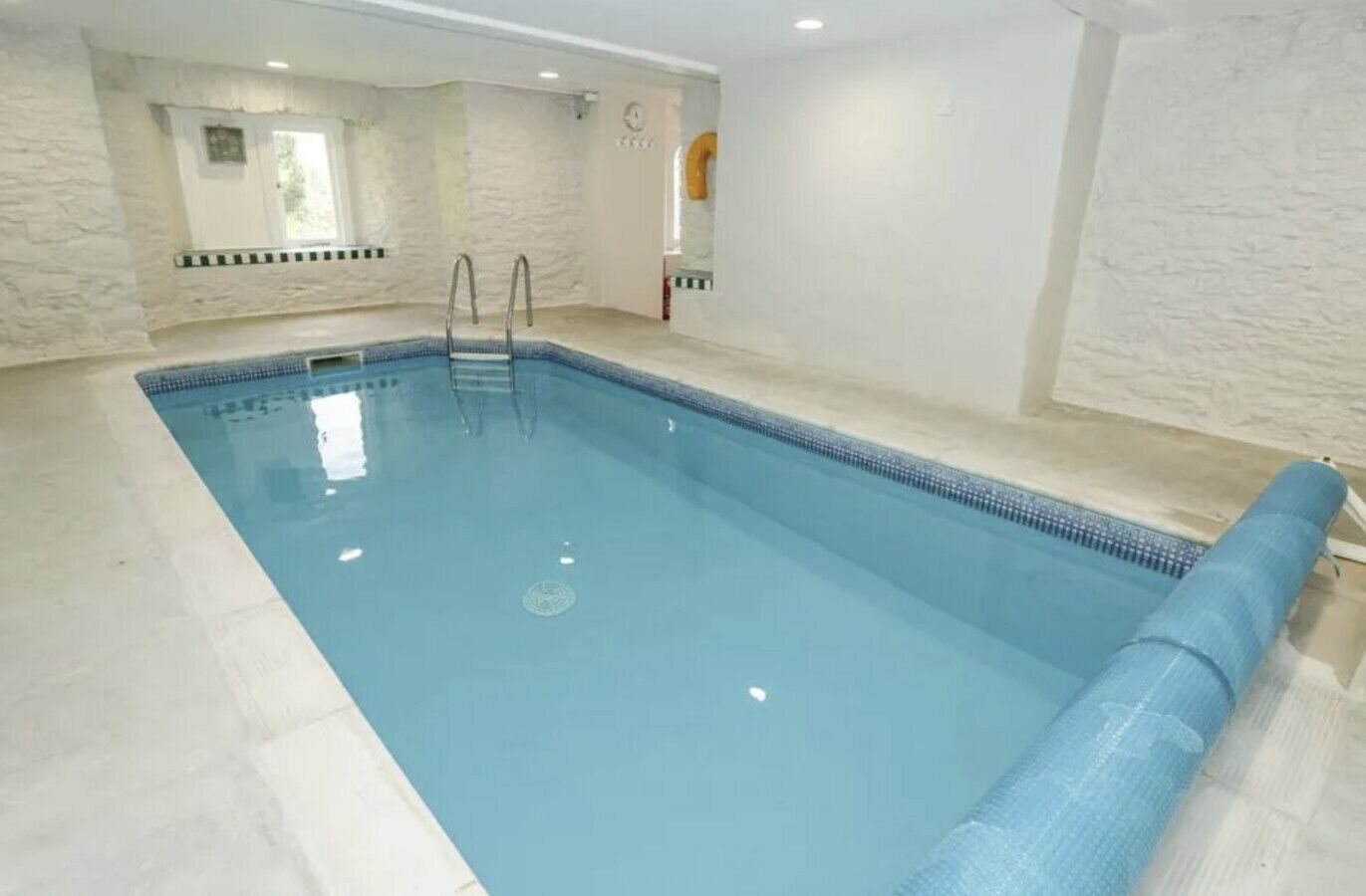An indoor swimming pool with clear water, a ladder, and a tiled floor.