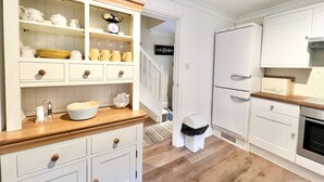Une cuisine avec des meubles blancs, un plan de travail en bois et un évier blanc. On y trouve une poubelle blanche et un réfrigérateur blanc.