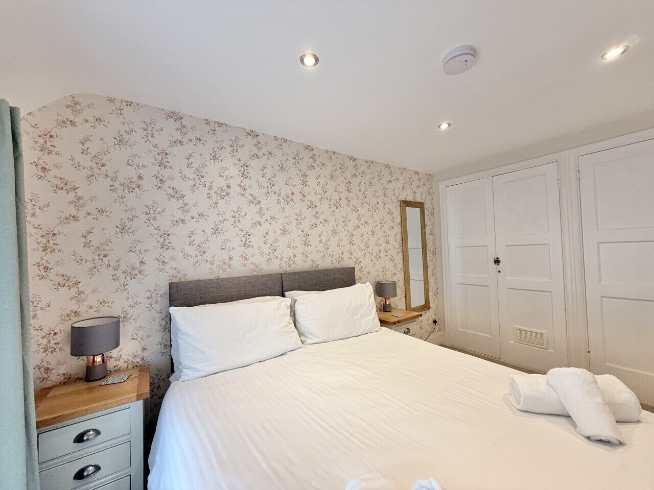 A neatly made bed with white linens, a bedside lamp, and a mirror on the wall.