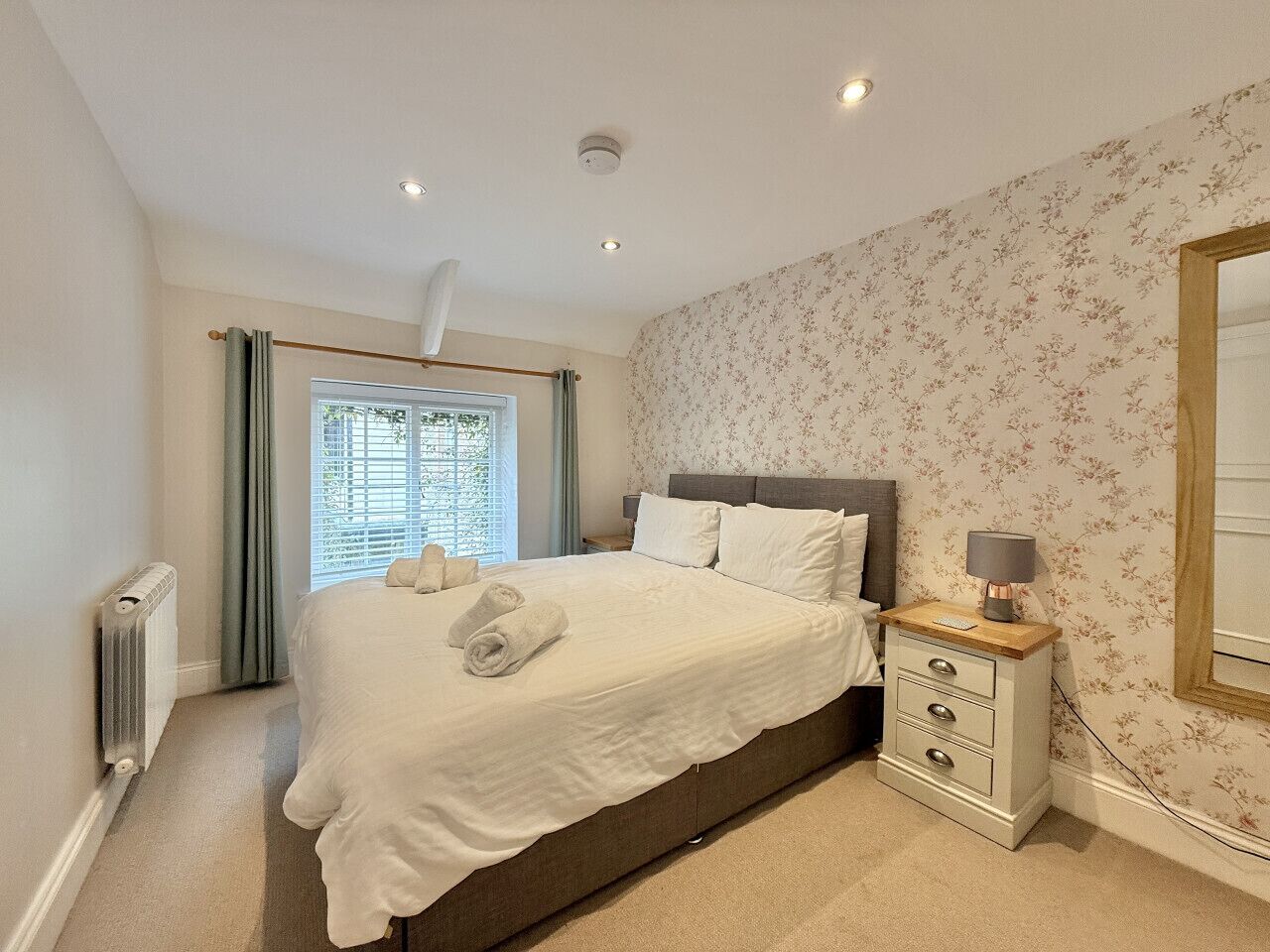 A neatly made bed with white linens, a bedside table with a lamp, and a window with curtains.