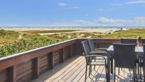 Eine Terrasse mit Sitzgelegenheiten mit Blick auf einen Strand und Dünen.