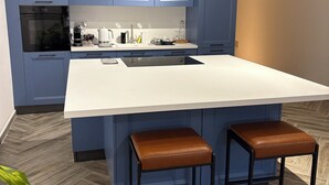 A modern kitchen with blue cabinets, a white countertop, and two stools.