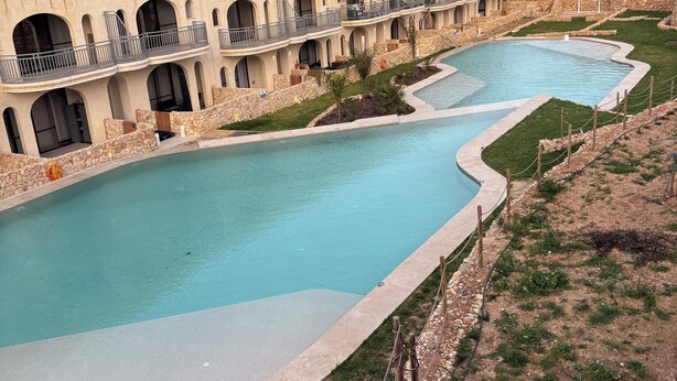 A hotel with multiple balconies, a swimming pool, and a stone retaining wall.