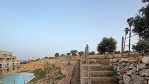 A stone staircase leading to a pool area, surrounded by a rocky landscape and a clear sky.
