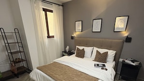 A bedroom with a large bed, a nightstand, a ladder, and a window with curtains.