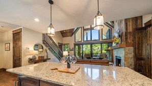 A spacious kitchen with a large granite island, wooden accents, and a stone fireplace.