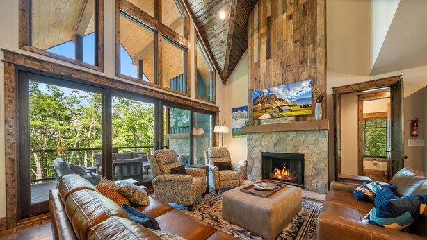 A spacious living room with a stone fireplace, leather sofas, and large windows offering a view of the outdoors.