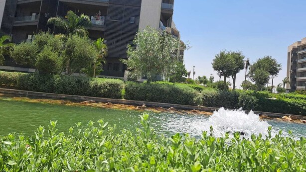 A modern building with balconies, surrounded by well-maintained greenery and a water feature. - 3-bedroom apartment in cool Cairo with WiFi, AC (Cairo)