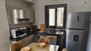 A modern kitchen with a dining table set for four, a refrigerator, and a microwave. - 3-bedroom apartment in cool Cairo with WiFi, AC (Cairo)