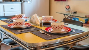 Une table à manger avec quatre tasses blanches à pois rouges, chacune accompagnée d’une soucoupe assortie, le tout posé sur des sets de table foncés.