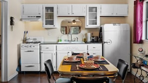 Une cuisine compacte avec des meubles blancs, une cuisinière, un réfrigérateur et une table à manger pour quatre personnes.