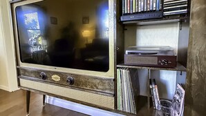 Un téléviseur ancien, posé sur un meuble en bois doté d’étagères où sont rangés des livres et des DVD.