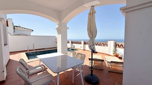Une terrasse avec une table, des chaises, une piscine et une vue sur la mer.