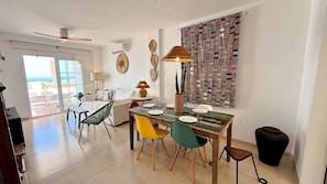 A dining area with a table set for four, a sofa, a patterned wall, and a view through a glass door.