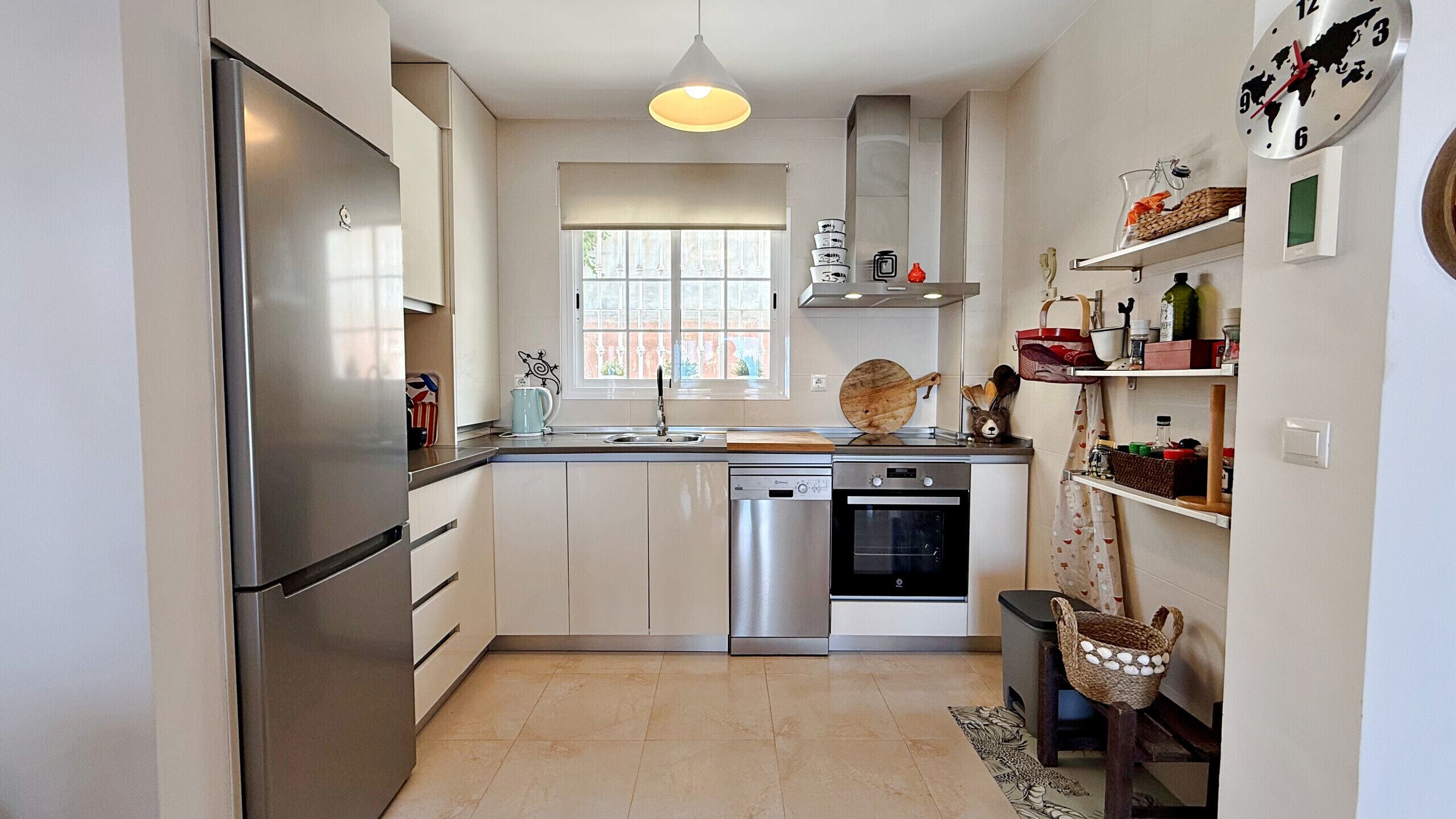 A modern kitchen with stainless steel appliances, a window, and a hanging light fixture.