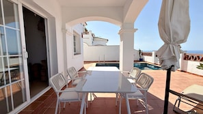 Une terrasse avec une piscine, des meubles blancs et une vue sur la mer.