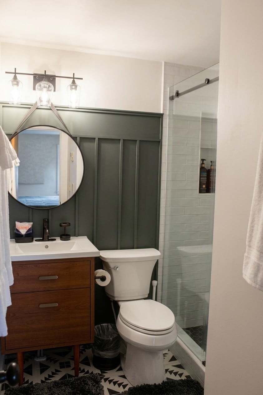 A bathroom with a toilet, a sink with a mirror, and a shower area.