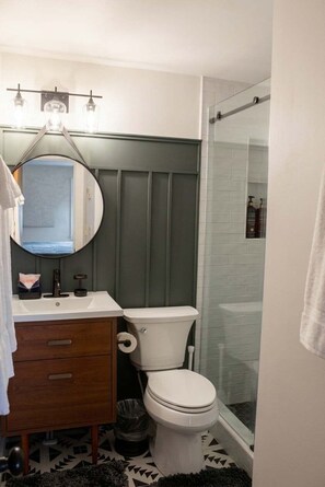 A bathroom with a toilet, a sink with a mirror, and a shower area. - Powderidge 15 Slope Side (Snowshoe)