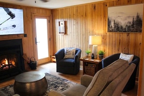 A cozy living room with a fireplace, a television, and a painting on the wall. - Powderidge 15 Slope Side (Snowshoe)
