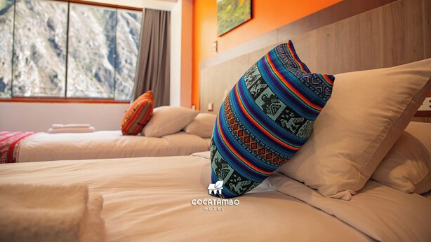 Une chambre d’hôtel avec deux lits, une grande fenêtre donnant sur les montagnes et des coussins aux couleurs vives.